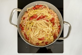 A pot of spaghetti is simmering on a stove, mixed with shrimp and cherry tomatoes