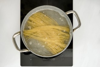 Long strands of pasta are submerged in boiling water inside a pot on an induction stovetop. The