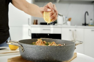 A person is preparing a seafood dish by squeezing fresh lemon juice into a skillet. The modern