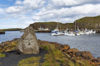 Face, engraved in a rock, boats in the harbour, rocky coastal landscape, Stykkisholmur,