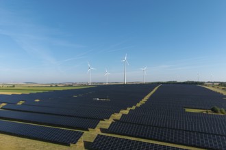 Field full of solar panels with wind turbines in the background under a clear sky, near Kitzingen,