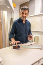 Architect using a digital tablet and choosing tiles in a home improvement store, holding a
