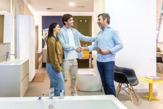 Couple shaking hands with salesman in a bathroom furniture store, finalizing purchase agreement