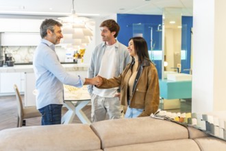 Young couple shaking hands with salesman after choosing new furniture for their apartment in a