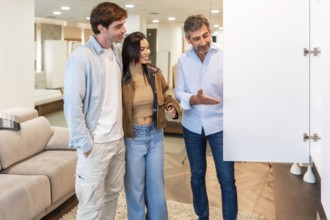 Smiling shop assistant showing a white cabinet door to a young couple, helping them choose