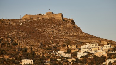 Settlement with castle on a hill in the warm light of the evening sun, surrounded by vegetation,
