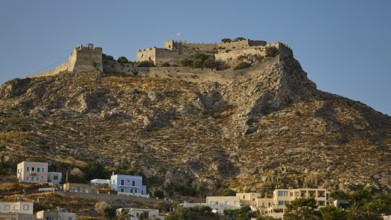 Historic castle on rocky hill under blue sky with coastal houses in the foreground, Pandeli Castle,
