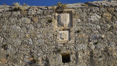 Medieval stone wall with engraved coats of arms and weathered engravings, coat of arms of Emery