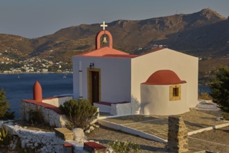 Chapel with red roof by the sea, surrounded by mountains and coastline, peaceful atmosphere,