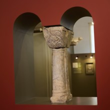 Part of an ancient stone column with relief-like decorations in a museum room, Archaeological