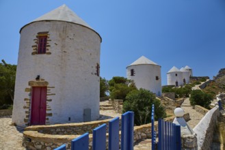 White windmills with red doors and fence under a blue sky on a sunny island, Pandeli Castle,