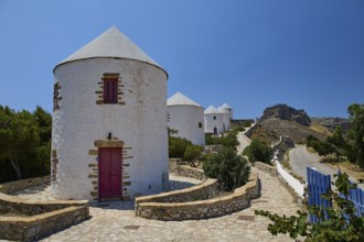 Whitewashed windmills with red doors along a stony path in the sun, Pandeli Castle, Castle, Leros