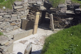Entrance to ancient ruins with stone walls surrounded by grass and moss, Skara Brae, Neolithic