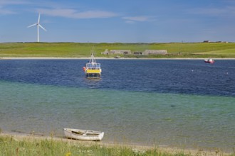 Colourful coastal landscape with boat, windmill and vast water under blue sky, Lambholm, Orkney