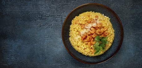 Risotto with shrimp, in a bowl, on a textured surface, with a side dish of fresh coriander,