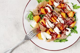 Salad with slices of ripe melon, prosciutto, mozzarella and fresh arugula, decorated with balsamic