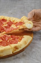 Delicious pepperoni pizza on a wooden board with a hand reaching for a slice. The crust is golden