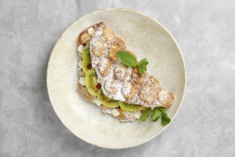 A delightful dessert featuring a crispy pastry shell filled with sliced kiwi, topped with powdered