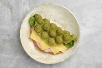 A creatively prepared sandwich features a vibrant green, fluffy waffle. Inside, layers of ham and