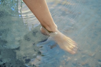 One foot dips into the refreshing lake water, creating gentle ripples on the surface. The bright