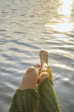 Enjoying a hot day at the lake, woman relaxes with her feet dipped in the calming water. The sun