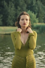 Bright sunlight casts a warm glow on a serene lake, where a woman poses gracefully in a green