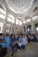 Indian woman pray between the white marble pillars around a marble elephant statue in the Adinath