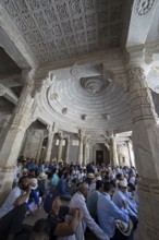 Indian men praying between the white marble pillars in the Adinath temple in Ranakpur, Jain temple,