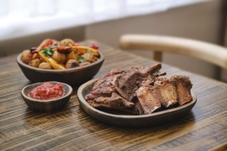 Tender roasted short beef ribs on a wooden table alongside a bowl of colorful roasted vegetables