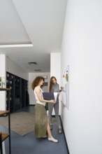 Two young women engage in a brainstorming session in a sleek office, discussing ideas on a