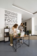 Two women engage in a collaborative work session within a contemporary office environment. The