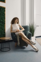 Woman relaxing in a stylish chair in a modern office space with greenery and natural light. She has