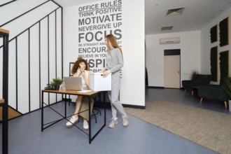 Woman speaks on the phone sitting in coworking and looks at her colleague in surprise, who brought