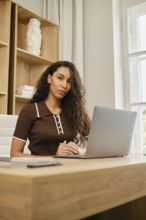 A young woman with curly hair works at the desk using a laptop. She was distracted from the screen