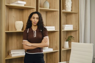 A confident businesswoman stands with arms crossed in a contemporary office space. The background