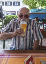 Senior citizen with sunglasses drinking a wheat beer in a beer garden, Upper Bavaria, Germany