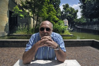 Portrait of an elderly gentleman with a beard and sunglasses sitting at a table, in the background