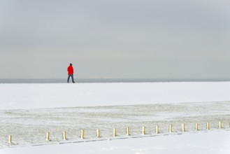 Winter day, onset of winter, snow on the North Sea coast, person walking over a dyke, North Sea,
