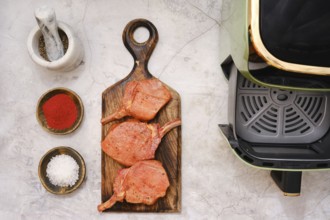 Three pork rib chops are placed on a wooden cutting board, surrounded by spices including paprika