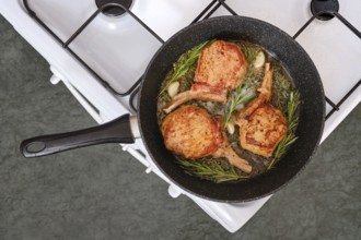 Pork rib roast sizzles in a skillet on the stovetop, surrounded by fragrant garlic and fresh herbs.
