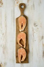 Three slices of fresh salmon steaks cross cut are arranged on a rustic wooden cutting board
