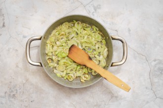 A pot filled with sautéed leek is on a countertop, showcasing a mix of fresh flavour being prepared