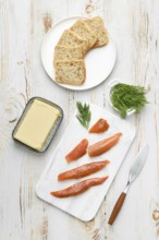 Herring caviar lay on a white cutting board beside a butter dish and sliced bread. Green dill adds