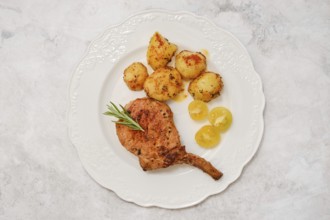 A roasted pork rib roast on a decorative white plate served with golden roasted potatoes and sweet