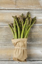 A bunch of fresh green asparagus stalks is wrapped in craft paper and tied with twine, placed on a