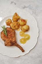 Delicious roasted pork rib roast is plated next to golden-brown crispy potatoes and tomato cherry.