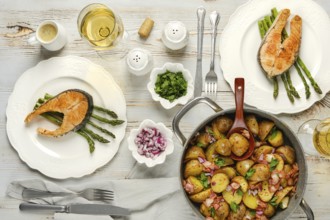 Two plates of grilled salmon served on asparagus sit alongside a pot of herbed potatoes. Fresh
