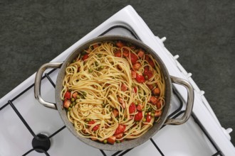 Overhead view of a pot filled with freshly cooked pasta with bacon and tomatoes on a stovetop. The