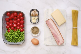 Overhead view of fresh cherry tomatoes, green peas, smoked bacon, garlic, parmesan cheese,