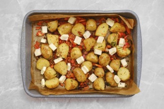 Golden roasted potatoes are arranged with pieces of feta cheese and herbs on a parchment in a